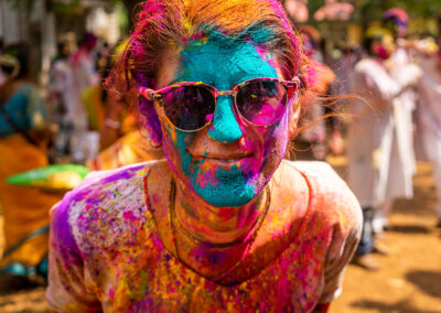 A young woman with sunglasses covered in color looking straight into the camera during the Indian festival of Holi